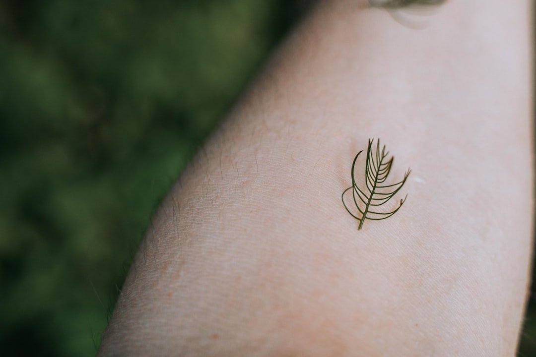 Delicate fine line botanical tattoo on inner forearm showing single needle technique